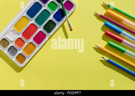 Forniture scolastiche. Una nuova serie di acquerelli di vernici, pennelli e penne a feltro, pennarelli, matite giacciono su una luce sfondo giallo. Strumenti per l'arte e disegno. Lay piatto. Spazio di copia Foto Stock