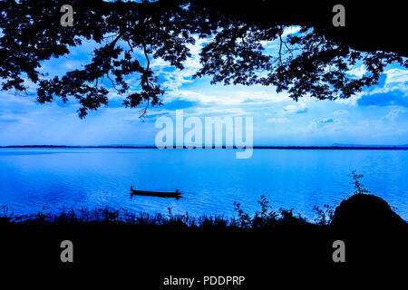 Un pescatore solitario si muove su un lago in una piccola barca come nella notte in tonalità blu Foto Stock