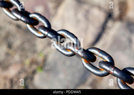 Una catena di metallo passa attraverso uno sfondo grigio di pietre per pavimentazione Foto Stock