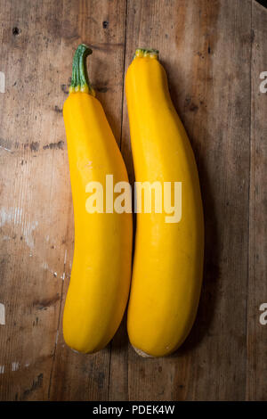 Una coppia di colore giallo o Zucchine Zucchine (Cucurbita pepo) su un piano di lavoro in legno in una cucina. Foto Stock