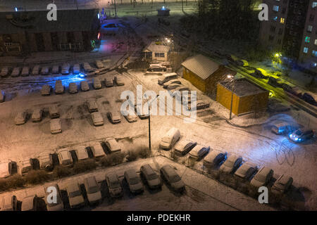 Parcheggio auto sotto luci colorate nella zona alla periferia della città sotto la neve per la Vigilia di Capodanno Foto Stock