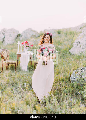 Allegro sposa con il bouquet. Ritratto a figura intera in montagna. Foto Stock