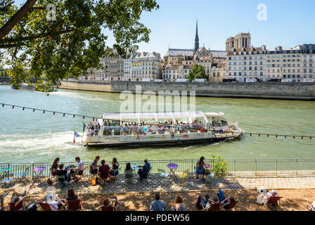 Persone in appoggio sulle sedie a sdraio lungo la Senna durante Paris-Plage evento estivo a Parigi, Francia, con la cattedrale di Notre Dame di Parigi in background. Foto Stock