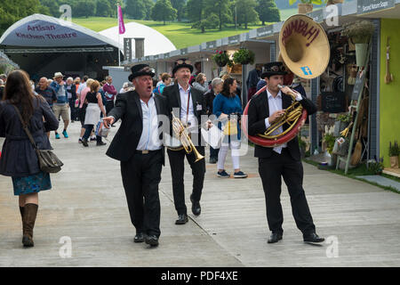 Maschio trio di musicisti vivace divertente persone, giocando & passeggiate sul viale degli stand commerciali - RHS Chatsworth Flower Show, Derbyshire, England, Regno Unito Foto Stock