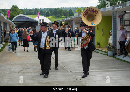 Maschio trio di musicisti vivace divertente persone, giocando & passeggiate sul viale degli stand commerciali - RHS Chatsworth Flower Show, Derbyshire, England, Regno Unito Foto Stock