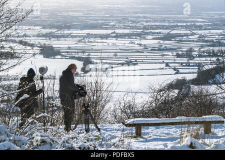 Un uomo della telecamera e operatore audio look-out attraverso la Nibberdale area di straordinaria bellezza naturale come la neve cade nello Yorkshire, Regno Unito Foto Stock