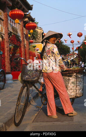 Donna che indossa floral camicia e pantaloni con coolie hat in piedi con la bicicletta in strada di Hoi An, Vietnam per solo uso editoriale Foto Stock