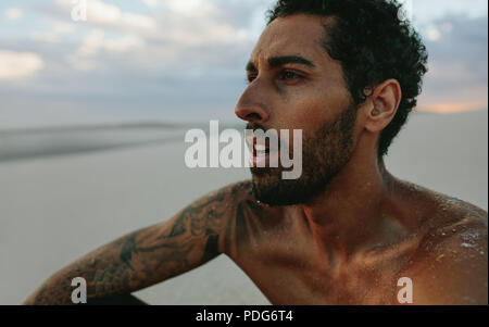 Chiusura del giovane uomo prendendo il resto dopo che esercitano nel deserto. Atleta maschio cercando stanchi dopo un intenso allenamento. Foto Stock