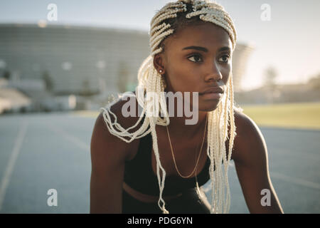 Close up di una femmina di runner pronti sul suo segni su una via di corsa. Sprinter cercando focalizzata pronto per la gara su pista. Foto Stock