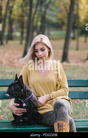 Bella e felice donna seduta sulla panchina nel parco con i suoi adorabili bulldog francese. Foto Stock