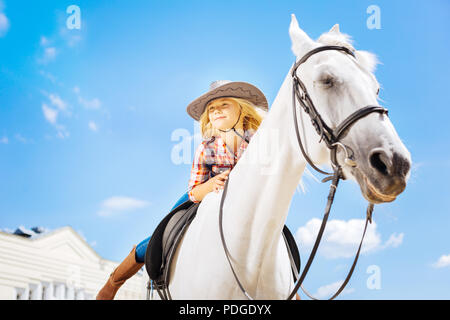 Bionda ragazza cowboy appoggiata al suo cavallo da corsa Foto Stock