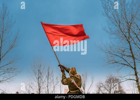 Gomel, Bielorussia - Novembre 26, 2016: giovane donna Re-enactor vestito come Soviet russo Red Army Soldier of World War II sventola una bandiera rossa in onore di vi Foto Stock