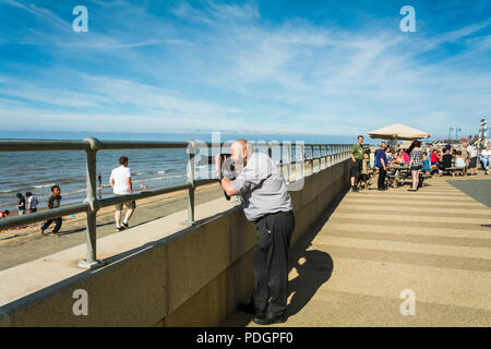 Un uomo barbuto di scattare le foto con una Nikon P900, Coolpix in una giornata di sole in spiaggia centrale di Prestatyn, nel Galles, UK. Foto Stock