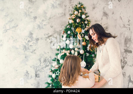 Donna con sua figlia in possesso di una scatola con un sacco di Natale decorazioni argento vicino all'albero di Natale. Vacanze di Natale concept Foto Stock