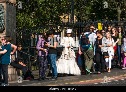 Edimburgo, Scozia, Regno Unito. Il 9 agosto 2018. Edinburgh Fringe Festival di Edimburgo, Scozia, Regno Unito. Su un soleggiato giorno del festival il centro della città è a pranzo con le persone e gli esecutori della frangia. Una donna che indossa performer Edwardian abiti sul cumulo tra la folla di pedoni Foto Stock