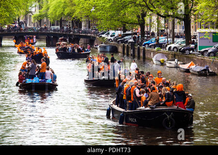 Amsterdam, Paesi Bassi - Aprile 2018: Barche sui canali di Amsterdam con la gente celebra il re del giorno in Paesi Bassi Foto Stock