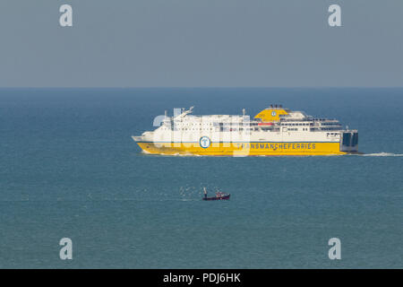 Traghetto e una barca da pesca in mare che mostra la differenza di dimensioni tra le due. Di colore giallo brillante traghetto blu verde mare cielo grigio. Viaggiare in direzioni opposte Foto Stock