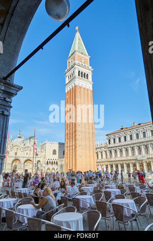 Piazza San Marco con il marciapiede tabella con le persone e i turisti si vede dal porticato, cielo blu in una soleggiata giornata estiva in Italia Foto Stock