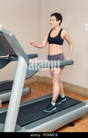 Ritratto di bella sorridente medio bianco invecchiato caucasian brunette donna con capelli corti facendo esercizi in palestra. Senior lady utilizzando race track Foto Stock