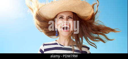 Felice donna elegante nel cappello di paglia jumping contro il cielo blu Foto Stock