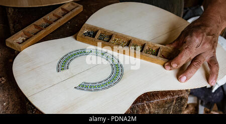 L'uomo mette tocchi di rifinitura sull'inserto intorno a un soundhole in un nuovo strumento Foto Stock