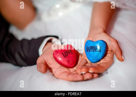 Le mani della sposa e lo sposo azienda pietre con amore e felicità parole Foto Stock