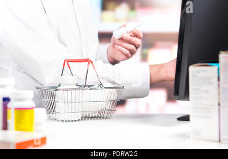 Farmacia cassiere o addetto al contatore. Il farmacista utilizzando un registratore di cassa. Speziale con flaconi portapillole nel carrello in drug store. Foto Stock