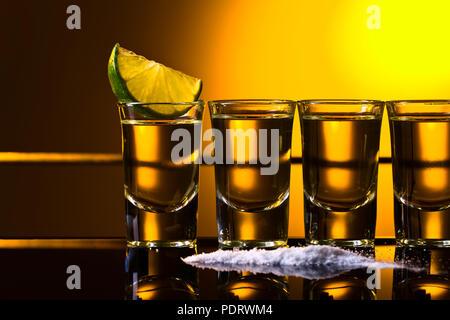 Mexican Gold Tequila in breve i vetri con calce e sale su sfondo riflettente. Foto Stock