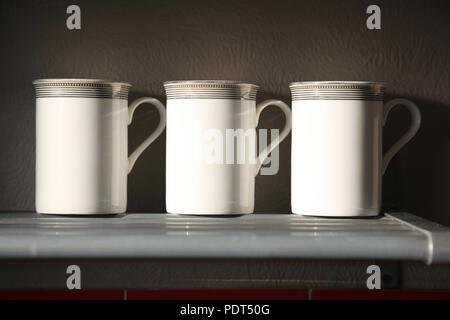 Tre bianchi tazze da caffè allineate su un ripiano di metallo. Foto Stock