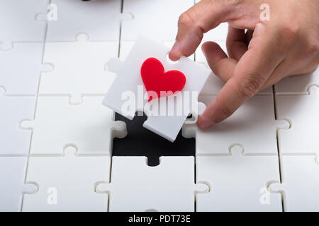 Persona ponendo mano ultimo pezzo con cuore rosso in bianco puzzle Foto Stock