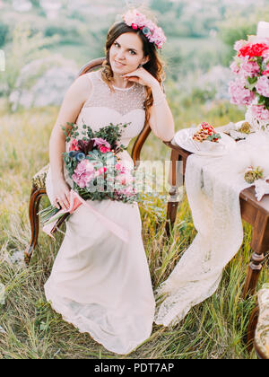 Close-up vista verticale della sposa sorridente con il mazzo di nozze seduta vicino alla tabella set. Foto Stock