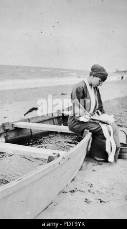 270 StateLibQld 1 66407 donna seduta su una barca spiaggiata la lettura di un libro, ca. 1925 Foto Stock