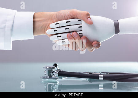 Il medico e il robot si stringono la mano su uno stetoscopio Foto Stock