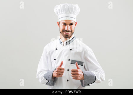 Lo chef sorridente che mostra il pollice in alto su sfondo grigio. Foto Stock