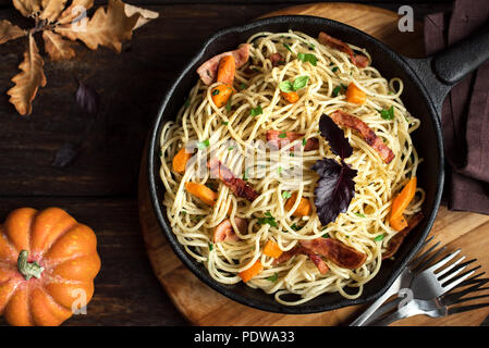 In autunno la pasta con zucca e pancetta in ghisa pan. Spaghetti fatti in casa di zucca sulla pasta di legno, copia dello spazio. In autunno il cibo. Foto Stock