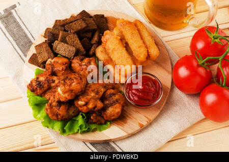 Ali fritte, pane secco e formaggio bastoni con boccale di birra, servite con salse su uno sfondo di legno Foto Stock