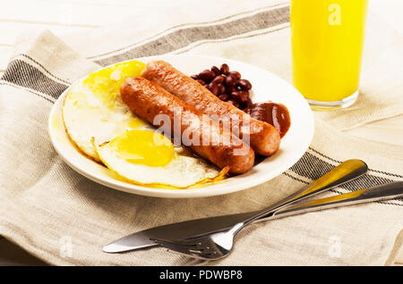 Una deliziosa prima colazione. Servita su un tavolo di legno con uova, salsicce, succo di arancia, coltello, forchetta. Foto Stock