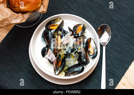 Cozze con cipolla e pancetta in salsa alla panna nel piatto fondo Foto Stock