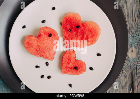 Fette di cocomero nella forma di cuore su vintage tavolo in legno. Vista superiore Foto Stock