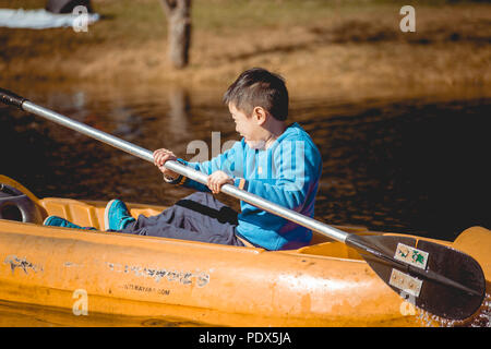 Ragazzo in sella a una barca su un lago con sfondo sfocato Foto Stock