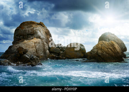 Paesaggio marino con rock in oceano, nuvole scure in cielo e sole brillante. Foto Stock