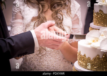 Close-up di una sposa giovane con le mani in mano il loro taglio torta nuziale. Foto Stock