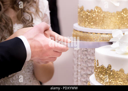 Close-up di una sposa giovane con le mani in mano il loro taglio torta nuziale. Foto Stock