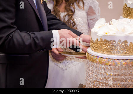 Close-up di una sposa giovane con le mani in mano il loro taglio torta nuziale. Foto Stock