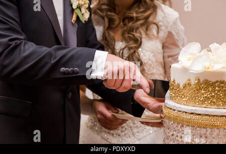 Close-up di una sposa giovane con le mani in mano il loro taglio torta nuziale. Foto Stock