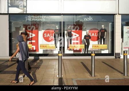 Due donne che indossano sciarpe di testa a piedi passato vendita segni di Dorothy Perkins e Wallis vetrina Foto Stock