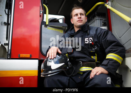 Foto del vigile del fuoco cercando l'uomo guarda lontano in seduta motore Fire Foto Stock