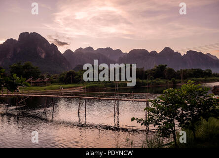 Glorioso tramonto sulle montagne che dominano il Vang Vieng affacciato sul Nam Song del fiume e del ponte di legno, Laos Foto Stock