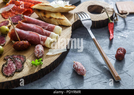 Tipiche tapas spagnole concetto. includono diverse fette di prosciutto, il chorizo, salame, bocce con olive e peperoni. Copyspace. Foto Stock