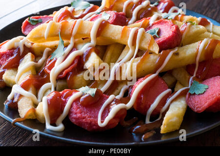 In casa Salchipapa peruviana le patatine fritte con le fette di salsiccia, ketchup e maionese. I cibi tradizionali. Foto Stock